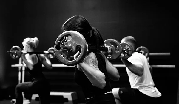 group training in gym doing squats with barbells on their back