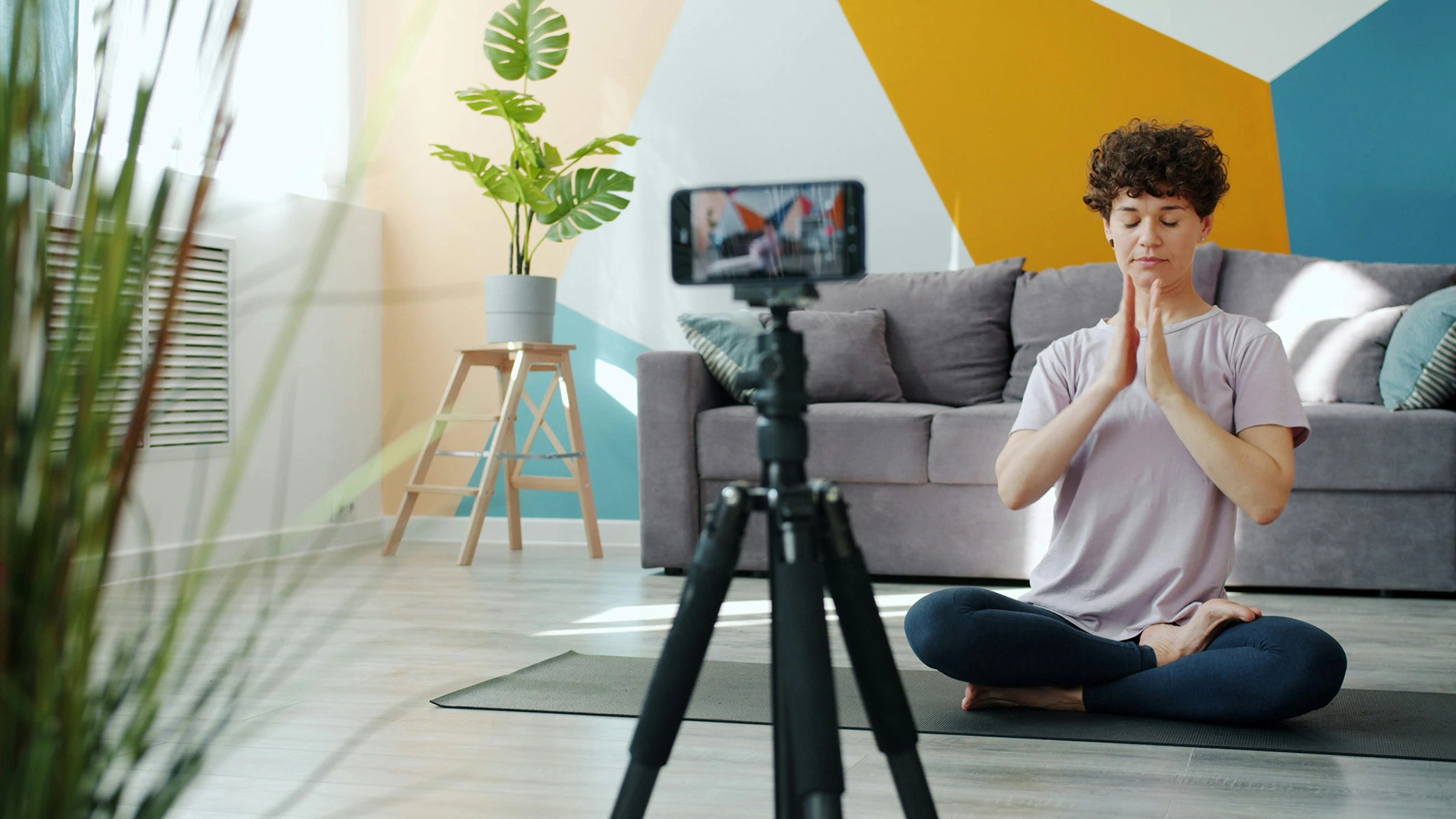 Virtual personal trainer recording a video for a lesson on a yoga mat in her living room
